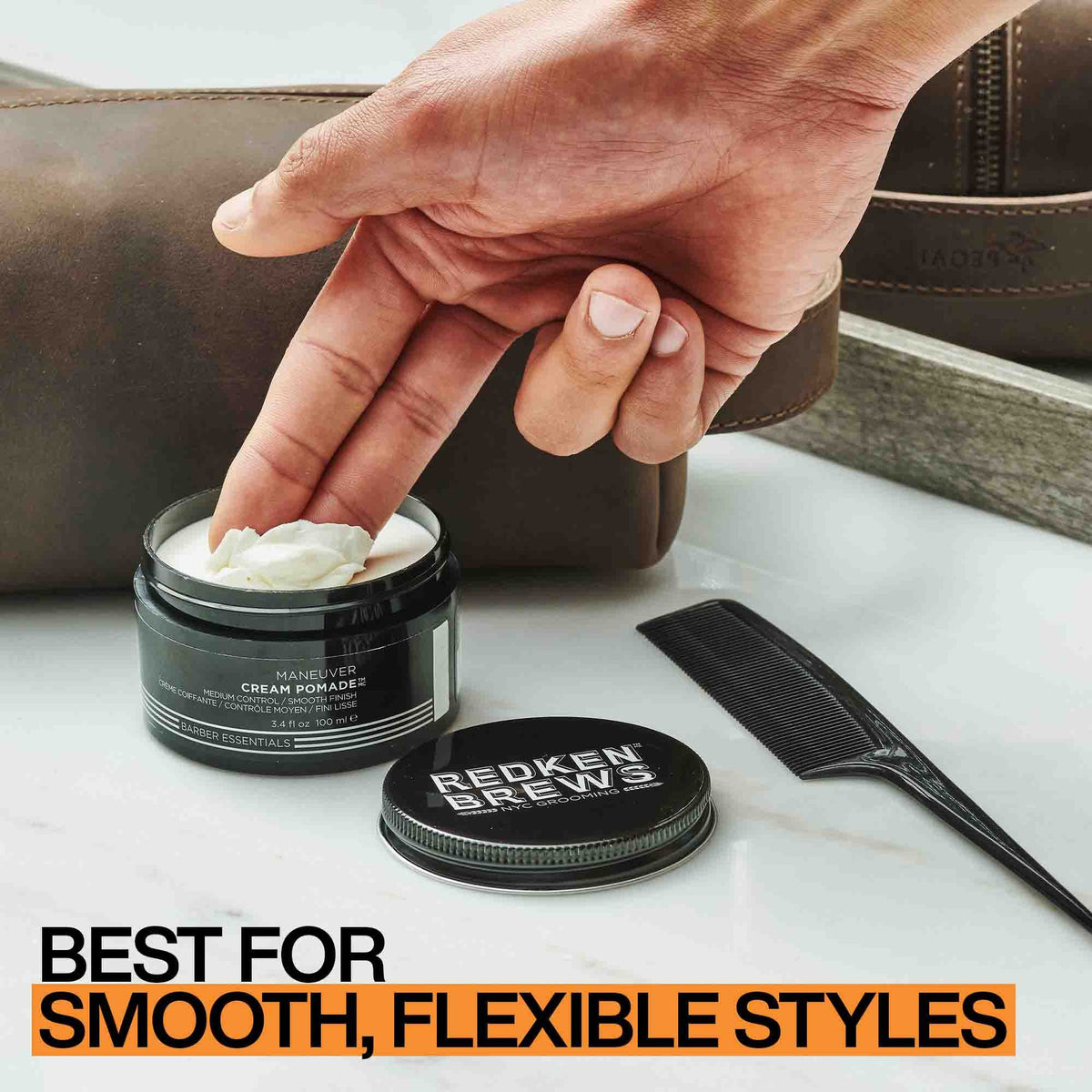 Fingers scooping Redken Brews Maneuver Cream Pomade from the jar, with a comb